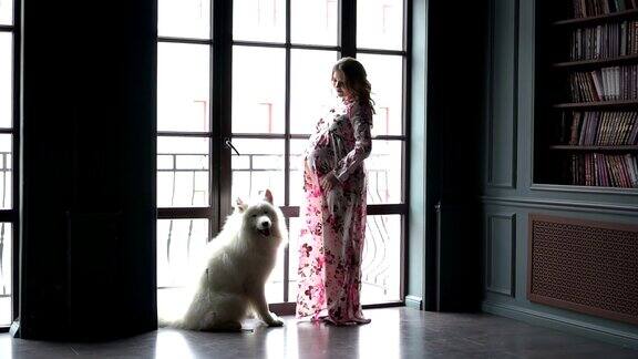 一个孕妇和她的狗站在窗边