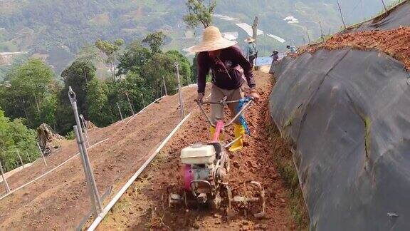 亚洲男性农民用手摇拖拉机在山坡上犁地