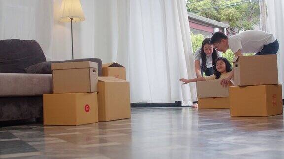 快乐的亚洲年轻家庭有乐趣的笑声搬进新家日本父母父母微笑着帮助兴奋的小女孩坐在纸板箱里新的财产和搬迁