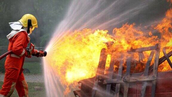 身穿消防服执行安全救援任务的勇敢的消防队员从消防水龙带中喷水扑灭爆裂燃烧的汽车上的噼啪火焰消防队员在危险训练区域救火
