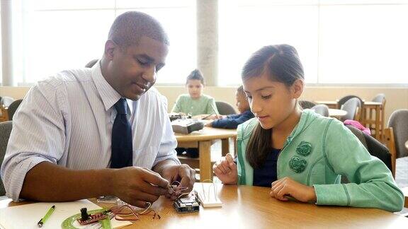 非裔美国中年教师帮助青春期前的学生使用电子元件