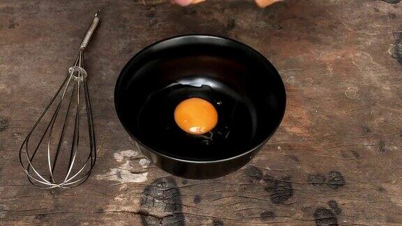 厨师的手在一个黑色的碗里打鸡蛋在一个旧的木头桌子上搅拌慢动作落地投篮