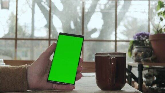 一个男人拿着一个绿色屏幕模型的手机喝着咖啡