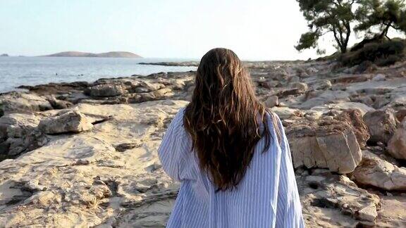 穿着衬衫和泳衣的女人在岩石嶙峋的海岸线上散步