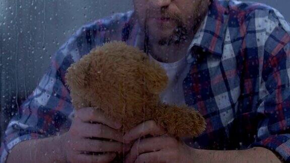 孤独的男人抱着泰迪熊躲在雨窗后离婚后失踪的孩子
