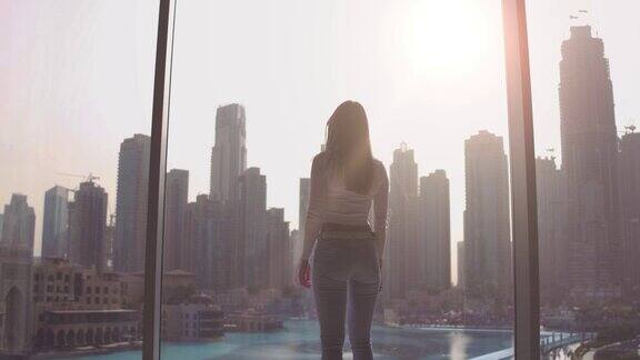 年轻女子在大窗户前拍照看着迪拜的城市建筑日落