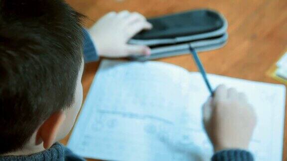 黑头发的男孩在家里用钢笔在笔记本上写字然后从盒子里拿出铅笔