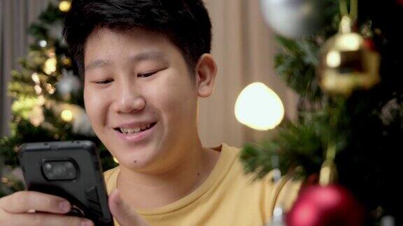 亚洲男孩在圣诞节的灯光背景下晚上在家玩手机游戏
