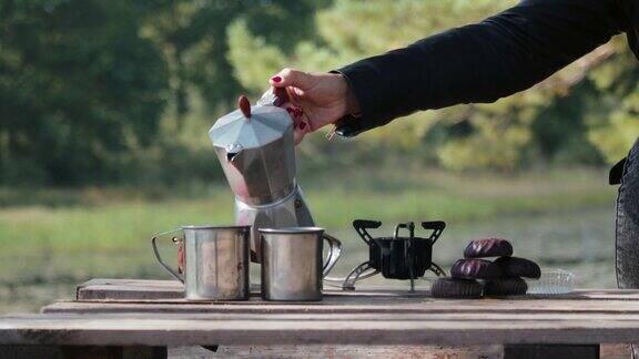 在美丽的自然背景下一个间歇泉咖啡壶与杯子和饮料一起放在炉子上在森林里呼吸新鲜空气