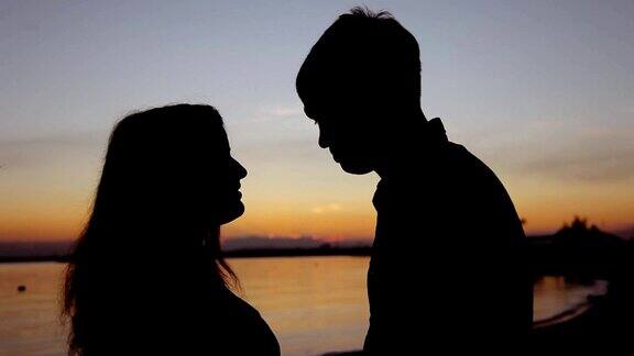 一对年轻的夫妇在海滩上做心形的手臂对着金色的夕阳