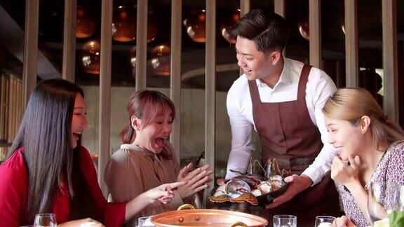 快乐的服务员带着火锅和海鲜在餐厅招待一群朋友