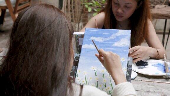 亚洲女子面朝画框坐下来在长方形的画框上画水彩画正用毛笔用白色的毛笔画雏菊花瓣给画面添上鲜艳的田野花朵