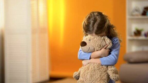 被遗弃的伤心的卷女孩抱着最喜欢的泰迪熊在孤儿院感觉悲伤