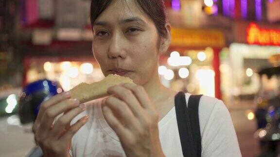 街头小吃-年轻女子在吃酥脆的煎饼在瑶华路曼谷泰国