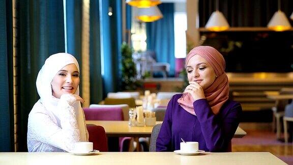 两个年轻漂亮的穆斯林妇女在一个咖啡馆聊天和大笑