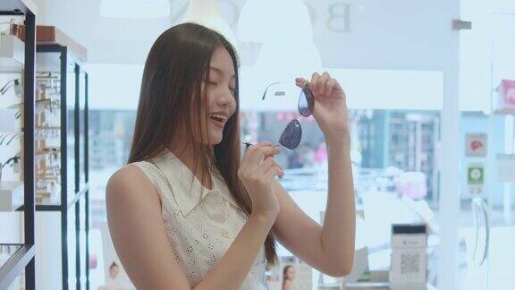 年轻的亚洲女人在光学商店挑选和试穿眼镜慢镜头