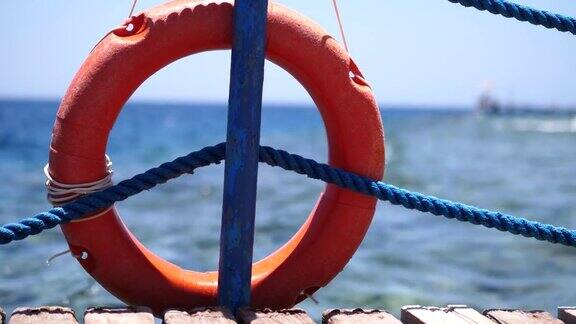 橙色的环形救生圈悬挂在码头上的杆子上背景是蓝天和在大海中游泳的人