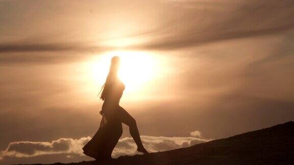 日落时分美丽的年轻女子在沙丘上跳东方肚皮舞轮廓