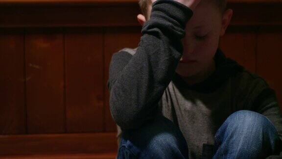 悲伤的小男孩独自坐在自己的房间里双手抱着头