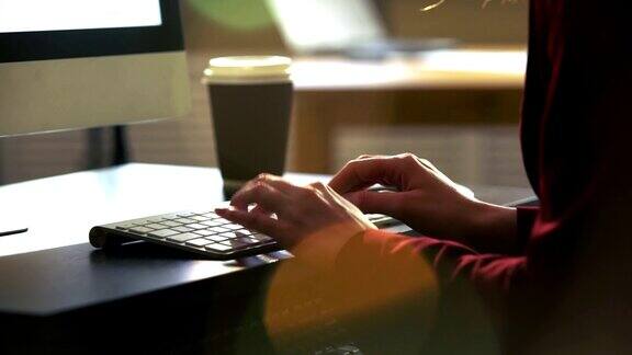 一个年轻女子在一张桌子前用电脑键盘工作太阳光的光学耀斑缓慢的运动