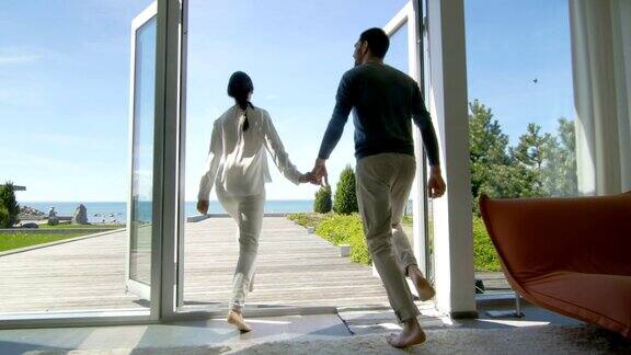 幸福的年轻夫妇牵着手跑出他们的家到阳台与海边的景色