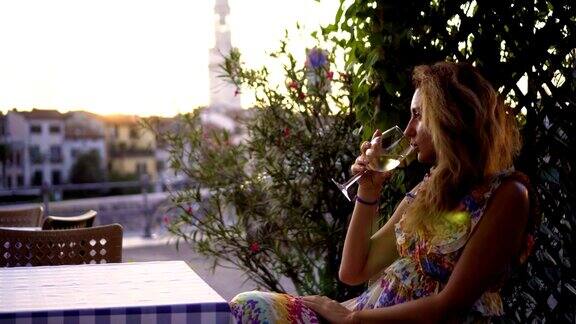 美丽的年轻女子喝着白葡萄酒在露台上欣赏日落捧着酒杯的漂亮女孩