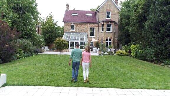 成熟的夫妇手牵着手穿过花园走向屋后