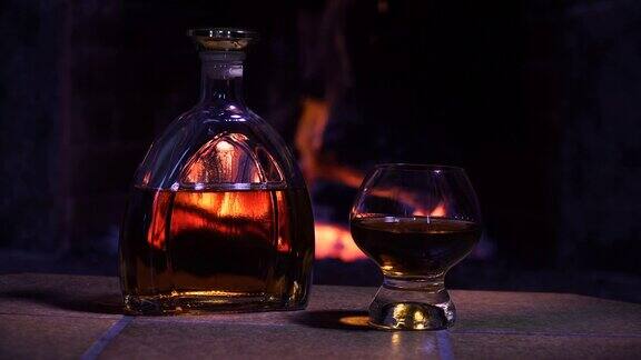 酒瓶和玻璃杯威士忌或干邑白兰地在壁炉的火的背景