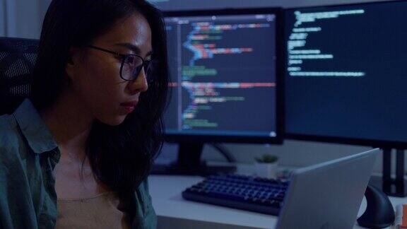 年轻的亚洲女性软件开发人员晚上坐在有多个屏幕的办公桌前远程工作用电脑写代码