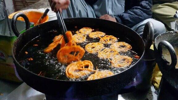 一名男子用平底锅煎和更换南亚和西亚最受欢迎的甜(Jalebi)的一面