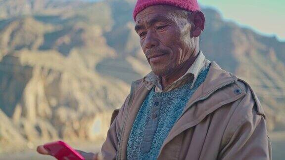 一个东亚老人站在贫瘠的土地上用智能手机