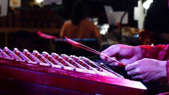 特写镜头聚焦在一场中国新年表演中一名男子用木棒弹奏古筝的双手