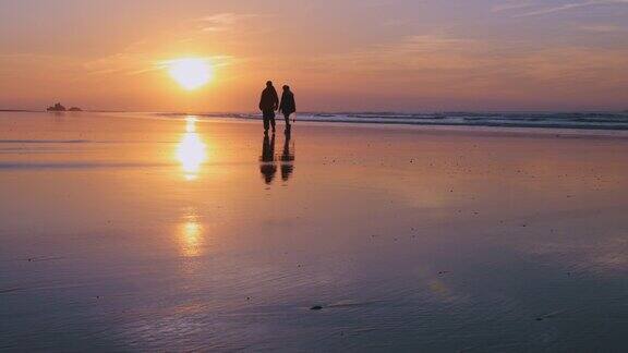 摩洛哥Essaouira彩色日落一对夫妇的剪影在海滩上散步4k宁静的氛围与太阳反射