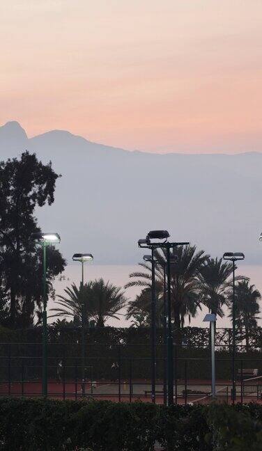 夕阳西下太阳落在山后人们在打网球环绕着大海和棕榈树垂直视频社交媒体