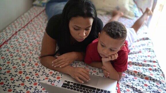 母亲和儿子在床上看笔记本电脑在家里