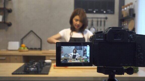 年轻的亚洲女人在厨房里给摄像机录像微笑的亚洲女人工作的食物博主概念与水果和蔬菜在厨房