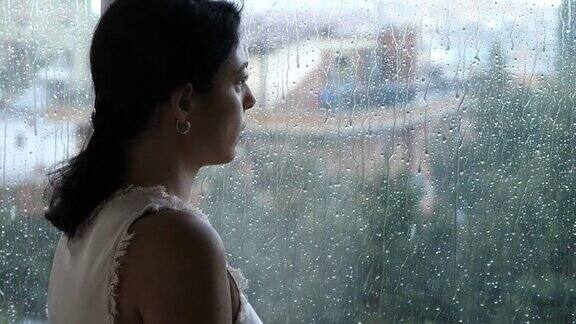 孤独忧郁下雨天女人站在窗前思念着她的前夫