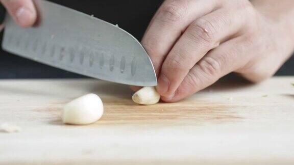 正前方的厨子用刀把大蒜切成薄片放在切菜板上