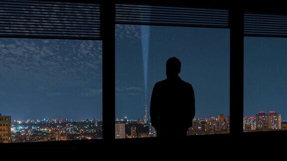 在城市的夜晚背景下这个男人站在靠近窗户的地方时间流逝