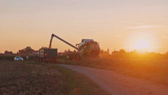 日落时分SLOMO联合收割机将谷物装载到拖拉机拖车中