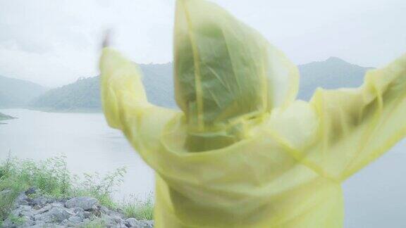 年轻的亚洲女人感到高兴玩雨而穿着雨衣站在湖边女性在雨天享受和放松的生活方式