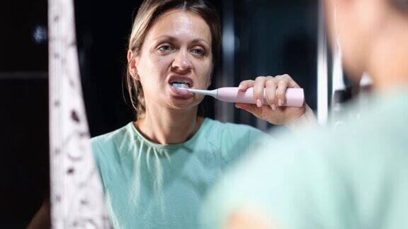 女人对着镜子用电动牙刷刷牙