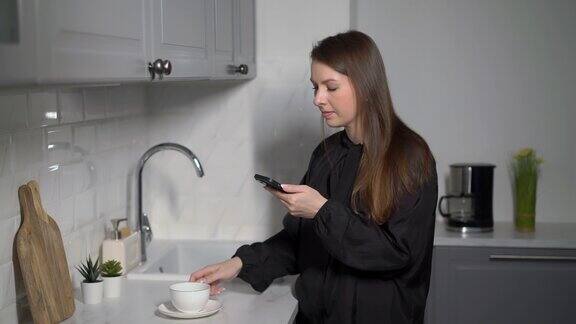 一个年轻的女人在厨房里用手机女孩手里拿着智能手机