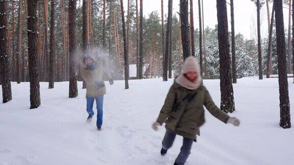 一对爱玩的情侣在寒假期间一起在雪林里蹦蹦跳跳、打雪仗