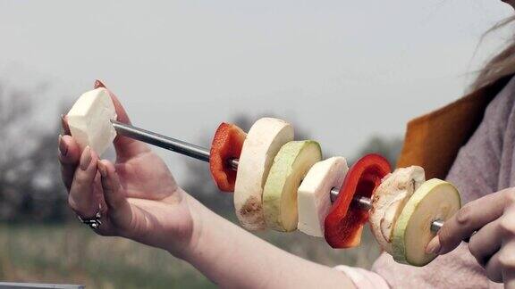女性手串蔬菜串在烤肉串在户外野餐