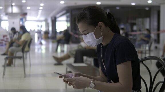 年轻女子拿着智能手机在杂货店购物戴着医用防护口罩保持社交距离