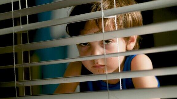 一个沉思的小男孩在夜晚透过窗户向外偷看