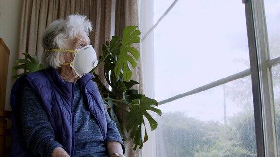 广角拍摄悲情的白种老年妇女戴着n95防护口罩望着窗外感到孤独预防COVIDSARSnCoV19冠状病毒猪流感H7N9流感疾病在寒冷和流感季节