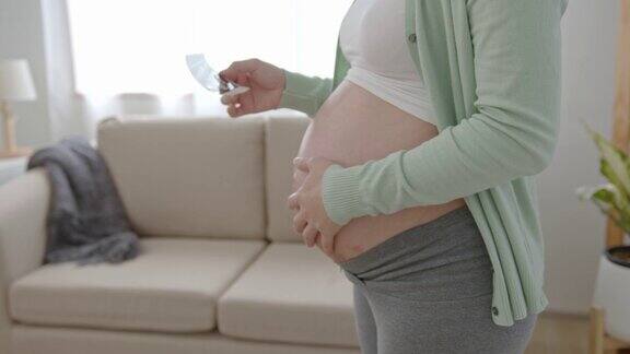 亚洲孕妇手拿超声图像在腹部在家里怀孕产妇准备和预期