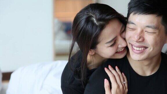 亚洲华人夫妇在床上拥抱拥抱微笑亲吻一起在早上笑